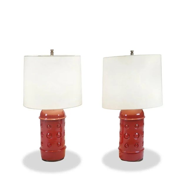 This pair of ceramic table lamps by Remains Lighting Company features a bold, sculptural form with a glossy red glaze and...