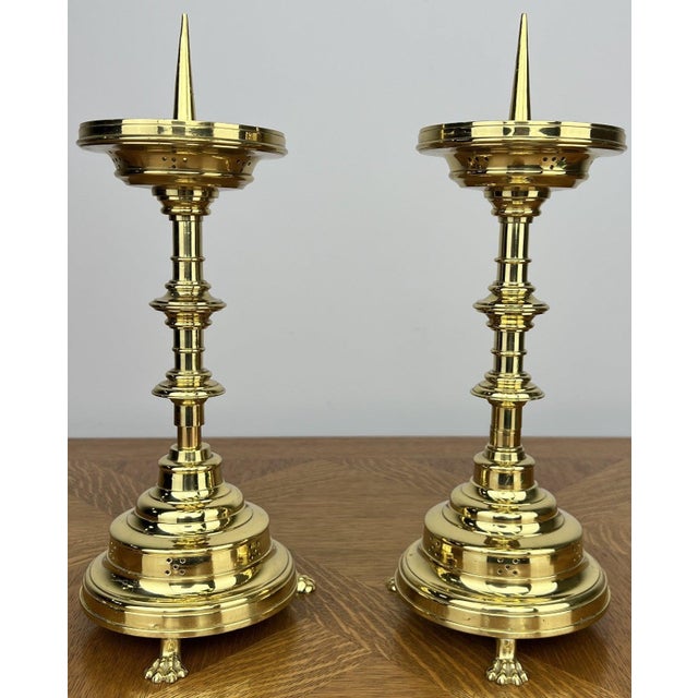 A striking pair of vintage brass candle holders featuring elegant turned stems, circular drip trays, and decorative claw...