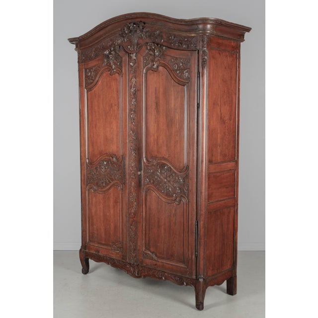 An early 19th century Louis XV country French bridal armoire from Normandy. Made of pine with fine hand-carving...