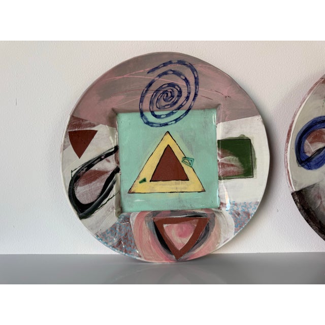 A dynamic pair of vintage handmade ceramic wall art plates by artist Larry H., dated 6.82. Each plate showcases a unique...