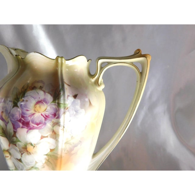 This is a pale yellow and white coffee pot with a very faded mark. It has a double handle design at the top, purple and...