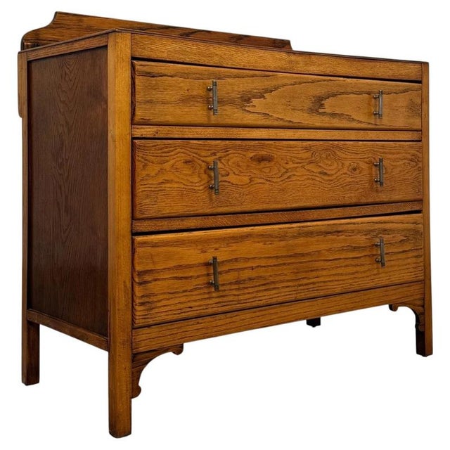 A charming early 20th-century English chest of drawers, well crafted from golden oak and distinguished by its warm...