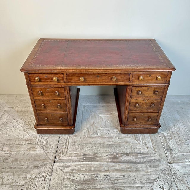 A Victorian Oak Pedestal Desk by Deighton & Dunthorne Featuring a gilt-tooled dark red leather writing surface. The upper...