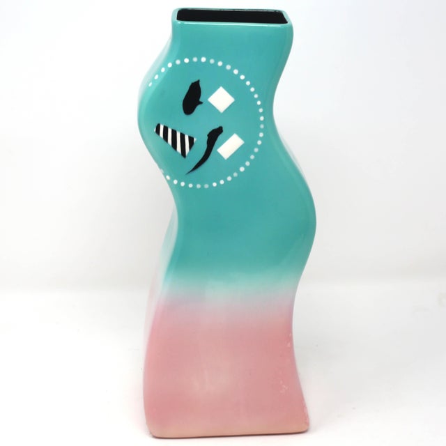 A vintage, handmade ceramic vase with a curvy form and black and white design over a blue to pink gradient background.