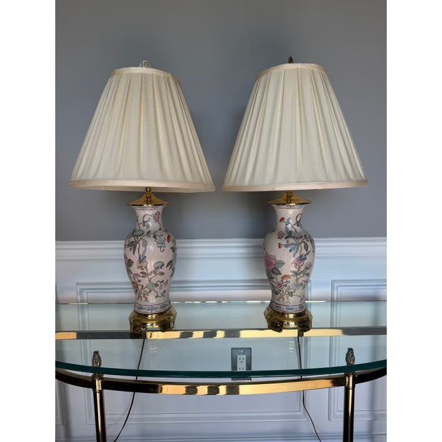 A charming pair of porcelain table lamps featuring a delicate hand-painted floral and bird motif in soft pastel tones,...