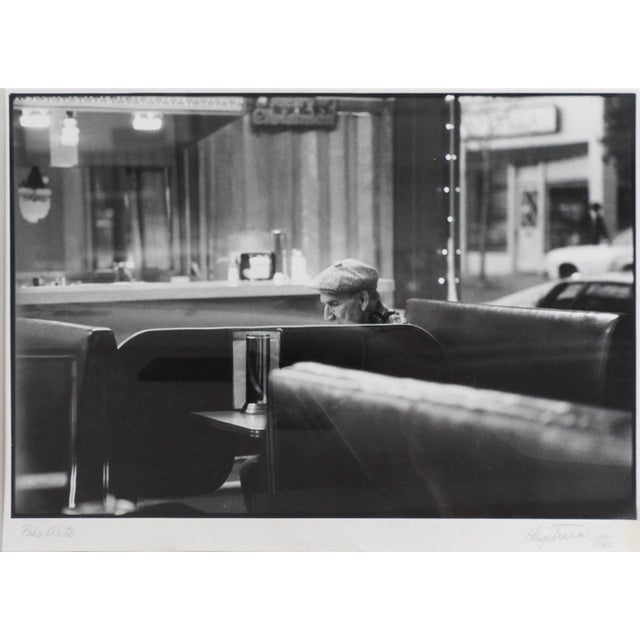 1982 black and white silver gelatin photograph of man in flat cap sitting in a diner. Signed illegibly, dated and titled...