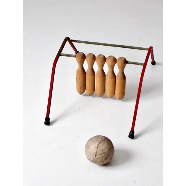 A charming mid-century tabletop bowling game featuring a red-painted metal frame with a back bar and five suspended wooden...