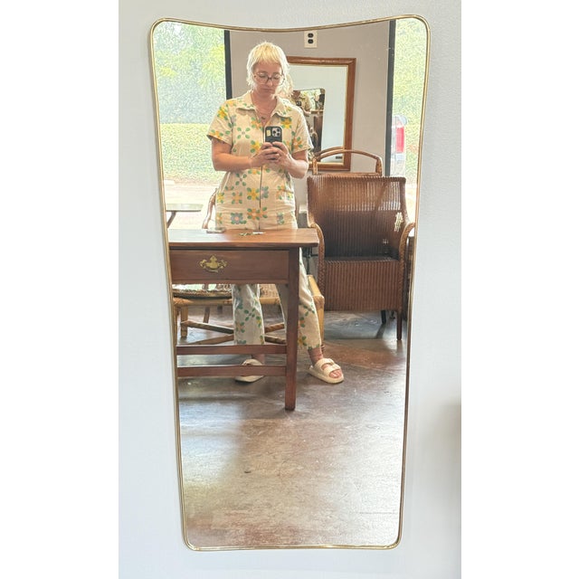 A fine Italian Modern wall mirror featuring a clean, Mid-Century design with an elegant, curved frame in brass, in the...