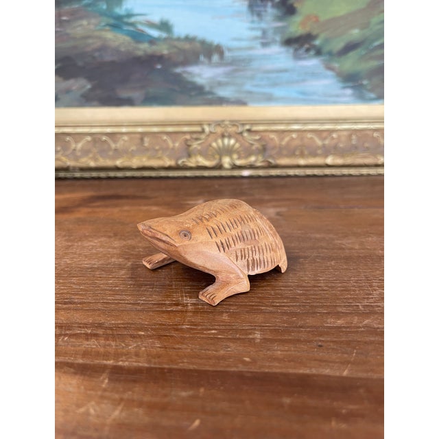 This hand-carved wooden frog sculpture features a charming, stylized form with deeply incised linear and chevron like...