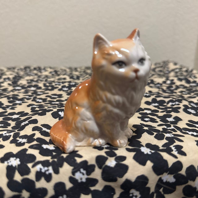 An adorable vintage porcelain figurine of a long-haired cat, likely a Persian or Angora breed, characterized by its fluffy...