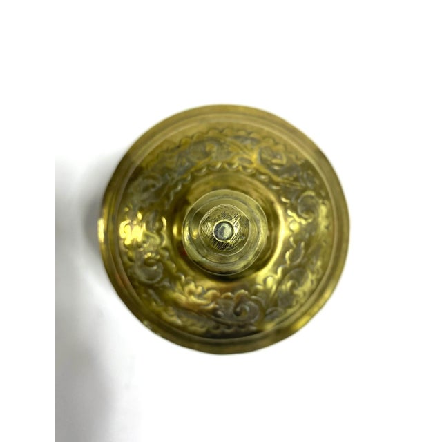 A richly etched vintage brass jar featuring ornate floral scrollwork, warm aged patina, and a sculptural finial lid....
