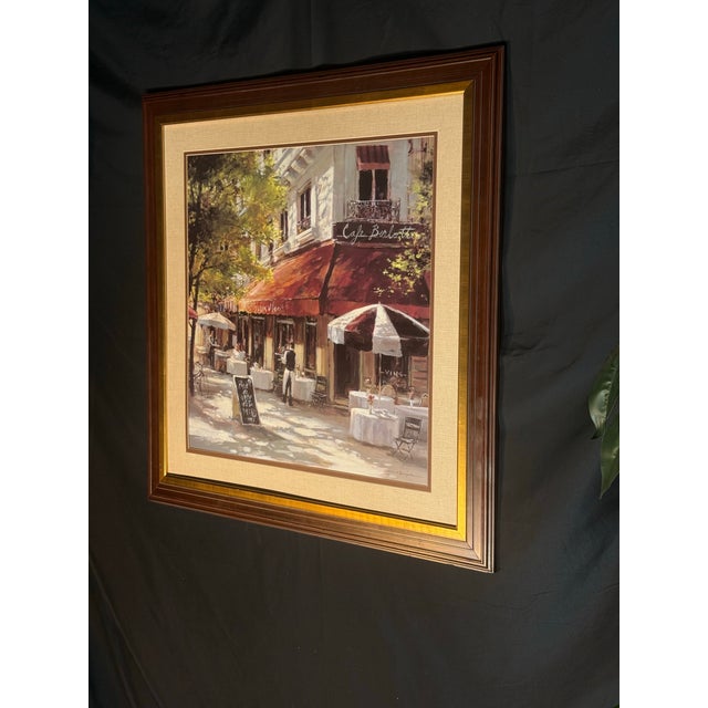 Framed print of "Cafe Berlotti" after the Canadian artist Brent Heighton: a sunlit Paris-style café corner with red...