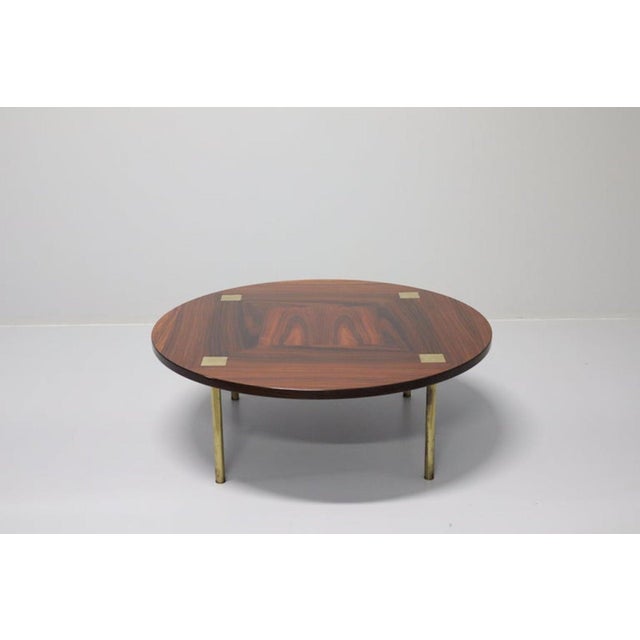 Round coffee or living room table with four brass legs, a wooden top, and brass details. The unique tabletop features a...