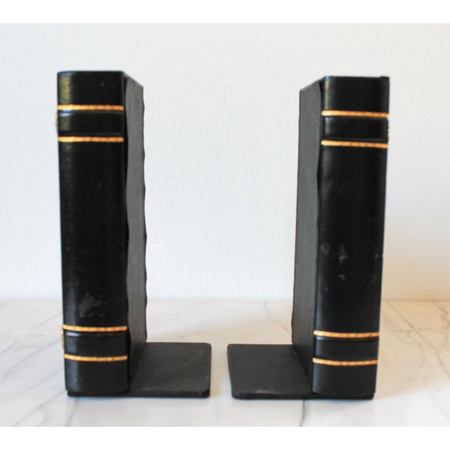 Pair of black leather wrapped faux book bookends with gold accents. No makers mark. Some age wear to leather. Pictured.