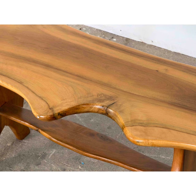 This bench is crafted from a solid slab of walnut with a live, freeform edge running along both long sides. The top rests...