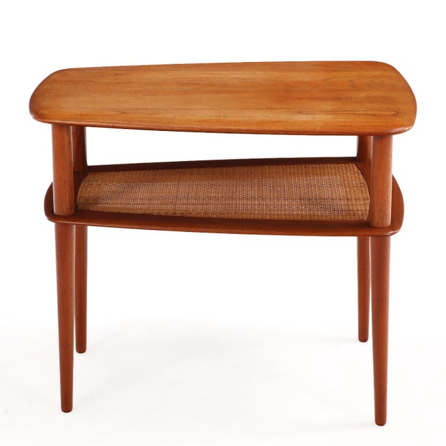 A finely crafted midcentury coffee/end table designed by Peter Hvidt, executed in solid teak with a woven cane lower tier....