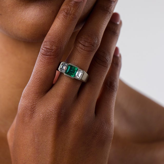 This exceptional Mid Century three-stone ring is centered by a square cut Colombian emerald weighing approximately 2.00...