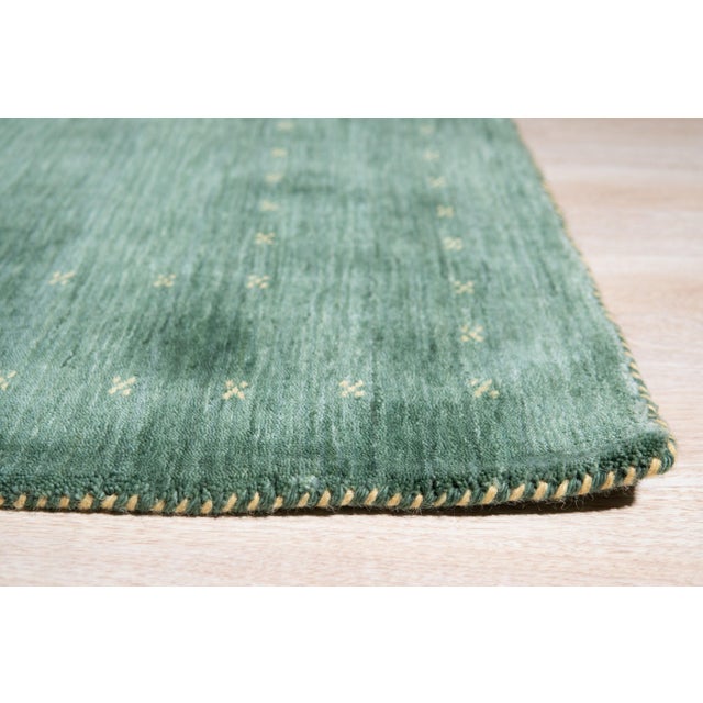 A hand-knotted wool rug, made in India and measuring 4' x 6'. Open green ground with restrained geometric detail — a quiet...