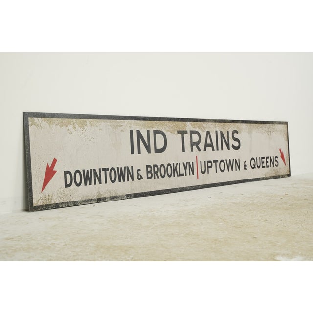 Reclaimed movie set street sign made of plastic foam board in white and black colors. The sign reads "IND TRAINS, DOWNTOWN...