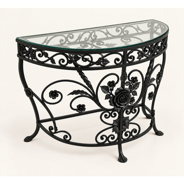An elegant demilune console with intricate scrolling floral metalwork and a glass top. The soft ivory finish lightens the...