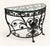 An elegant demilune console with intricate scrolling floral metalwork and a glass top. The soft ivory finish lightens the...