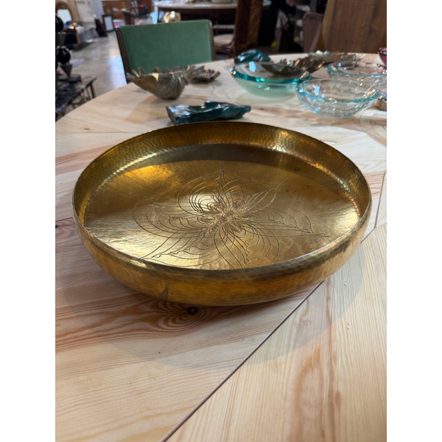 A striking vintage hand-hammered brass centerpiece bowl from the 1970s, featuring a broad circular form with a gently...