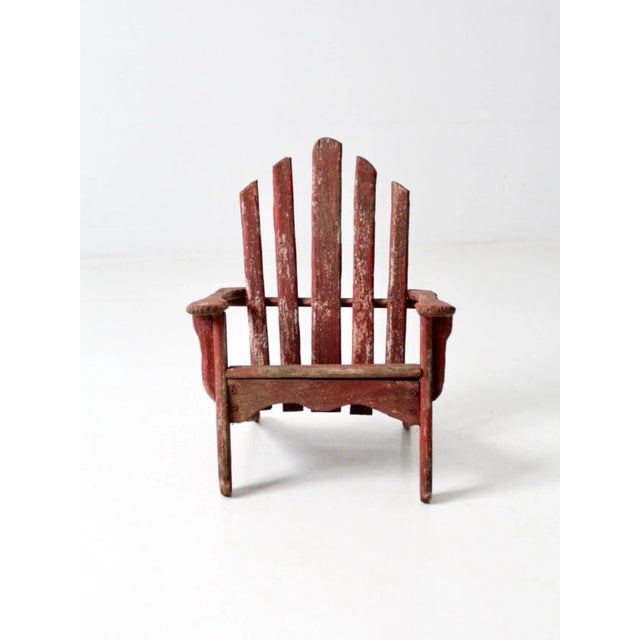 Vintage children’s Adirondack chair in rustic red, featuring the classic slat wood construction and low, angled...