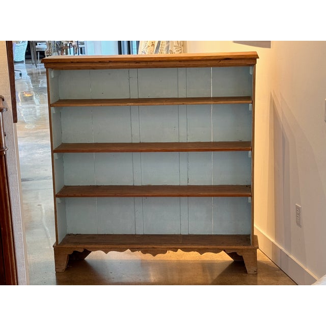 A country pine open bookcase with three fixed shelves above a shaped, scalloped apron resting on bracket feet. The honey-...