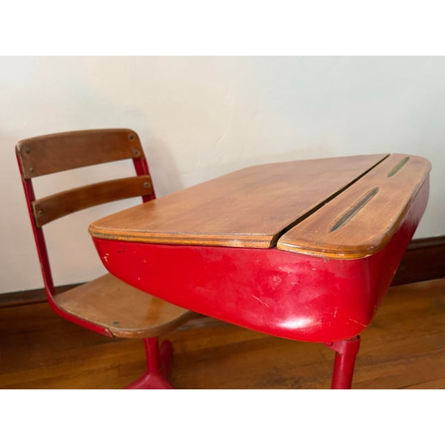 Midcentury children's school desk with a wooden writing top and a pencil groove. The frame is red painted metal and the...