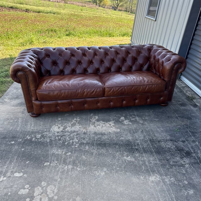 Vintage button tufted brown leather chesterfield sofa with two loose seat cushions. Turned wood bun feet. Rolled arms with...