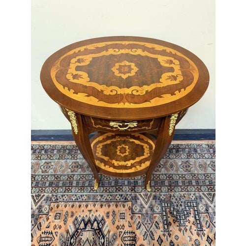 Beautiful oval side table featuring fine parquetry inlay with floral and urn motifs and ornate brass mounts. The curved...