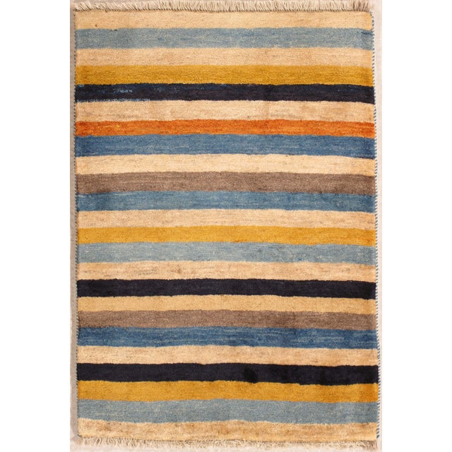 Hand-knotted Persian Gabbeh wool rug featuring a field of horizontal stripes in blue, ivory, mustard, brown, and orange...