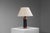 This distinctive table lamp combines the warmth of solid teak with the refined character of black leather, creating a bold...