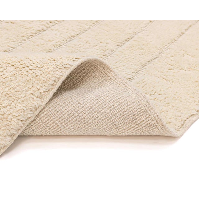 Sophisticated hand-knotted wool rug with a subtle hand-woven geometric symmetry in a tranquil Ivory hue, creating an...