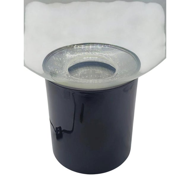 This extraordinary table lamp, stands out for its contrast in form and colour. Indeed, the shade is formed from a...