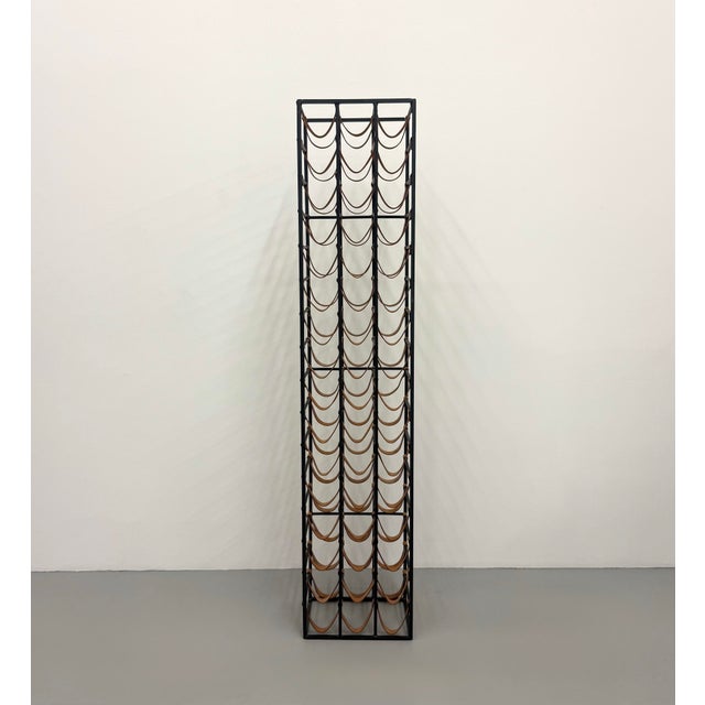 A sleek contemporary floor wine rack featuring a black metal frame with natural leather sling supports designed to cradle...