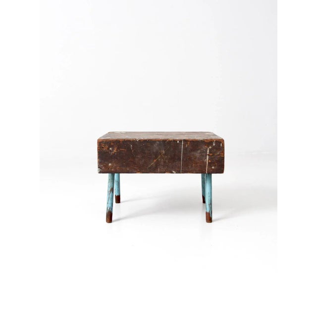 Rustic vintage wooden stool with a hand-crafted box-style top and splayed blue legs. The piece shows charming natural wear...
