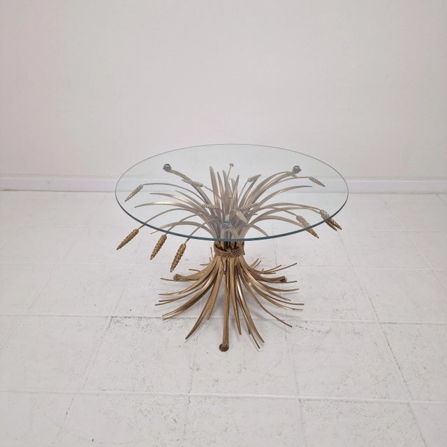 A striking Hollywood Regency-style coffee table from the 1970s, featuring a sculptural gilded “Sheaf of Wheat” base — an...