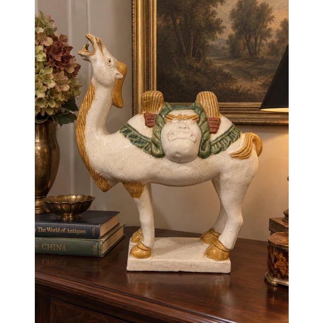 A substantial vintage Chinese ceramic camel sculpture inspired by Tang Dynasty funerary figures. The camel is modeled with...
