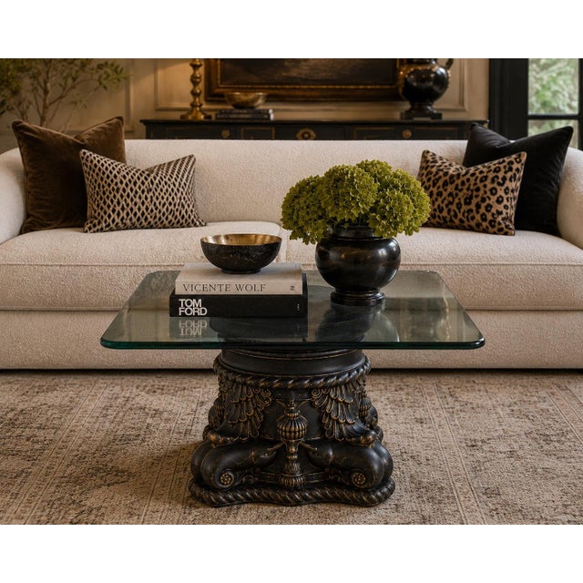 A dramatic Italian neoclassical revival cocktail table featuring a richly sculpted pedestal base finished in matte...