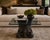 A dramatic Italian neoclassical revival cocktail table featuring a richly sculpted pedestal base finished in matte...