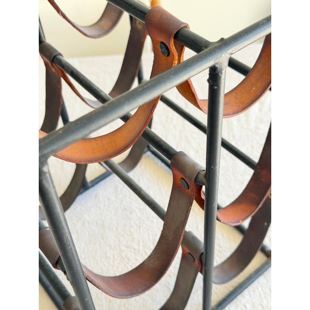 Striking mid century modern wine rack by Arthur Umanoff, featuring a black iron cube frame with saddle leather sling...
