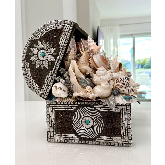 A striking shell‑encrusted treasure chest sculpture, handcrafted with an intricate assemblage of natural seashells, coral...