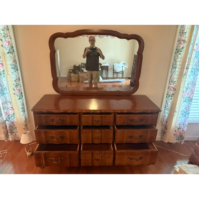 A vintage solid cherry wood French Provincial style dresser featuring nine drawers in a serpentine configuration with...