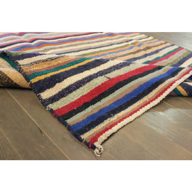 A hand-knotted Kilim rug with a stripe design on a multi-color field. Accents of blue, ivory, red, green and black...