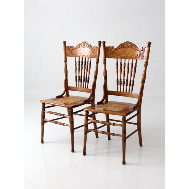 Pair of antique Victorian pressed-back cane chairs featuring ornate floral carvings, decorative scrollwork, turned spindle...