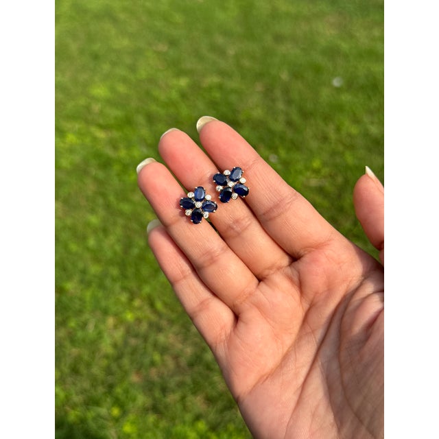 These 3.91-carat oval-cut blue sapphire and diamond flower cluster stud earrings are crafted in 14K yellow gold. Each deep...