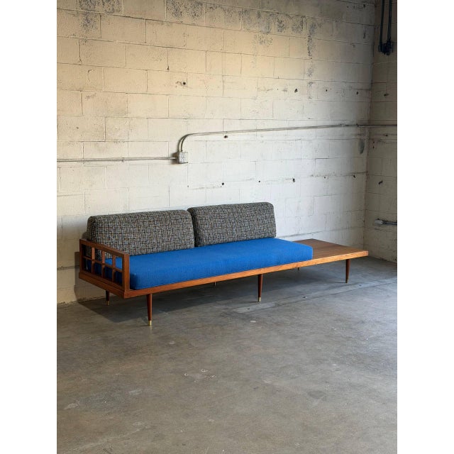 This striking long sofa features a built-in side table and an open slatted armrest. Its asymmetrical profile creates a...