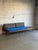 This striking long sofa features a built-in side table and an open slatted armrest. Its asymmetrical profile creates a...