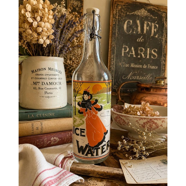 Vintage clear glass swing-top bottle decorated with a beautifully rendered Art Nouveau-style illustration of an elegantly...